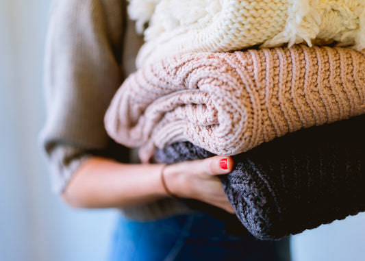 woman carrying a stack of winter sweaters
