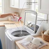 A top-loading washing machine in a bright kitchen setting with a hand pouring powder from a bottle into the open drum. Text callouts read 'no preservatives; no fillers', 'prevents buildup', 'all temperatures', and 'no filters'.